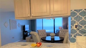 A kitchen with a marble countertop, a dining area with a table and chairs, and a view of the ocean through large windows. - Ocean Front Condo in New Smyrna Beach FL (New Smyrna Beach)