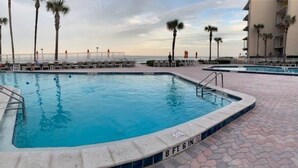 A swimming pool with a tiled edge, a lifeguard stand, and palm trees in the background. - Ocean Front Condo in New Smyrna Beach FL (New Smyrna Beach)