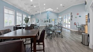 Un vaste espace dédié à la salle à manger, avec une longue table en bois et des chaises, entouré de grandes fenêtres et doté d’un plafond avec des luminaires encastrés.