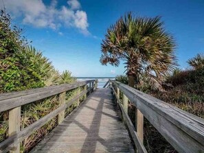 A wooden boardwalk leading to a beach with palm trees and ocean views.