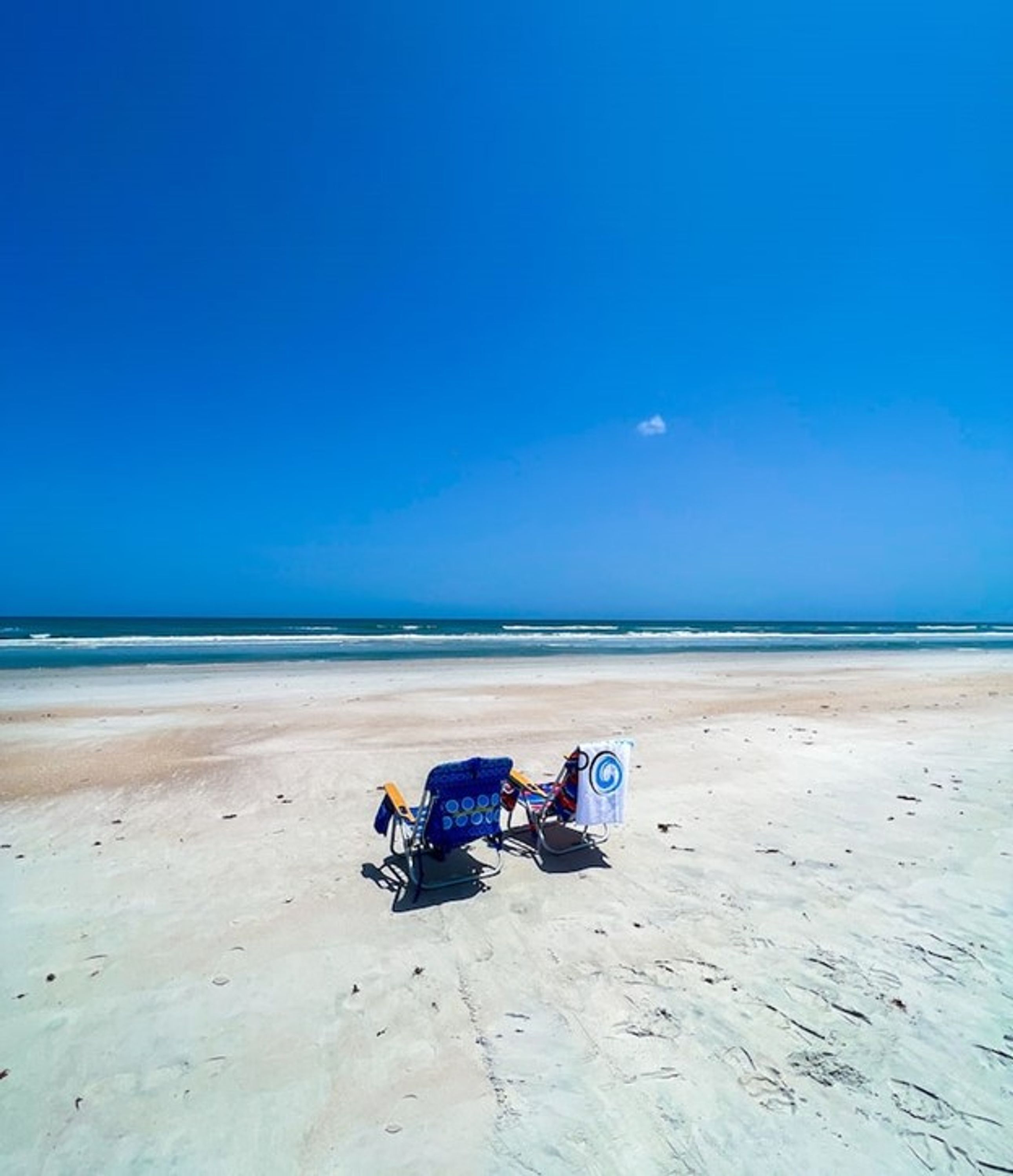 A beach with two beach chairs and a towel.