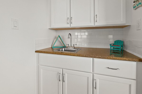 A kitchen with white cabinets, a stainless steel sink, and a teal Adirondack chair.