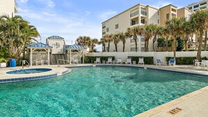 A clear swimming pool with lounge chairs and palm trees, surrounded by a building with multiple floors and balconies. - Oceanview 3 Bedroom Condo New Smyrna Beach FL (New Smyrna Beach)