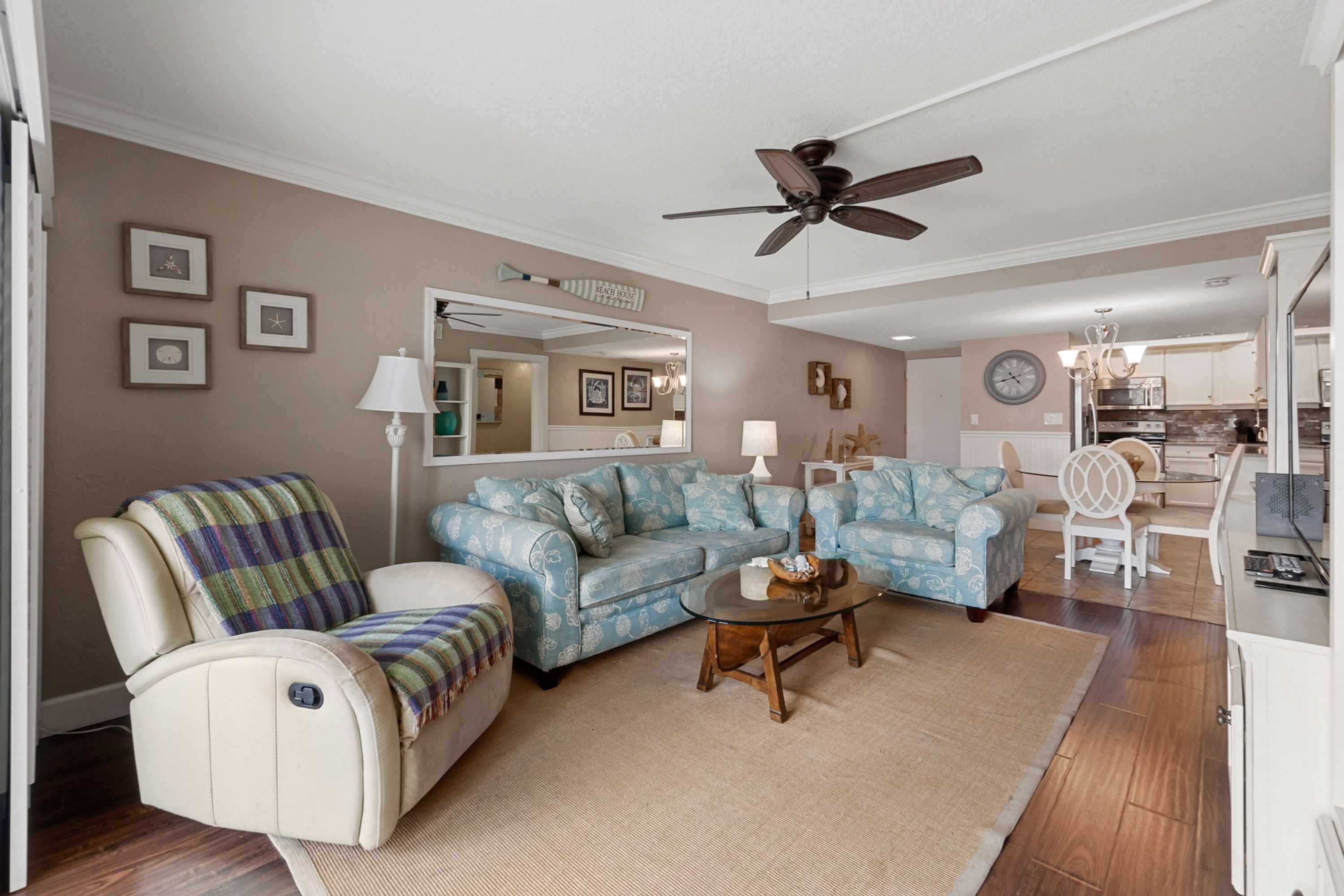 A living room with a sofa, armchair, and a coffee table. There is a ceiling fan, a lamp, and a clock on the wall.