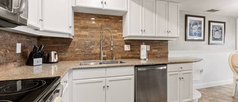 A modern kitchen with white cabinets, a stainless steel dishwasher, and a granite countertop.