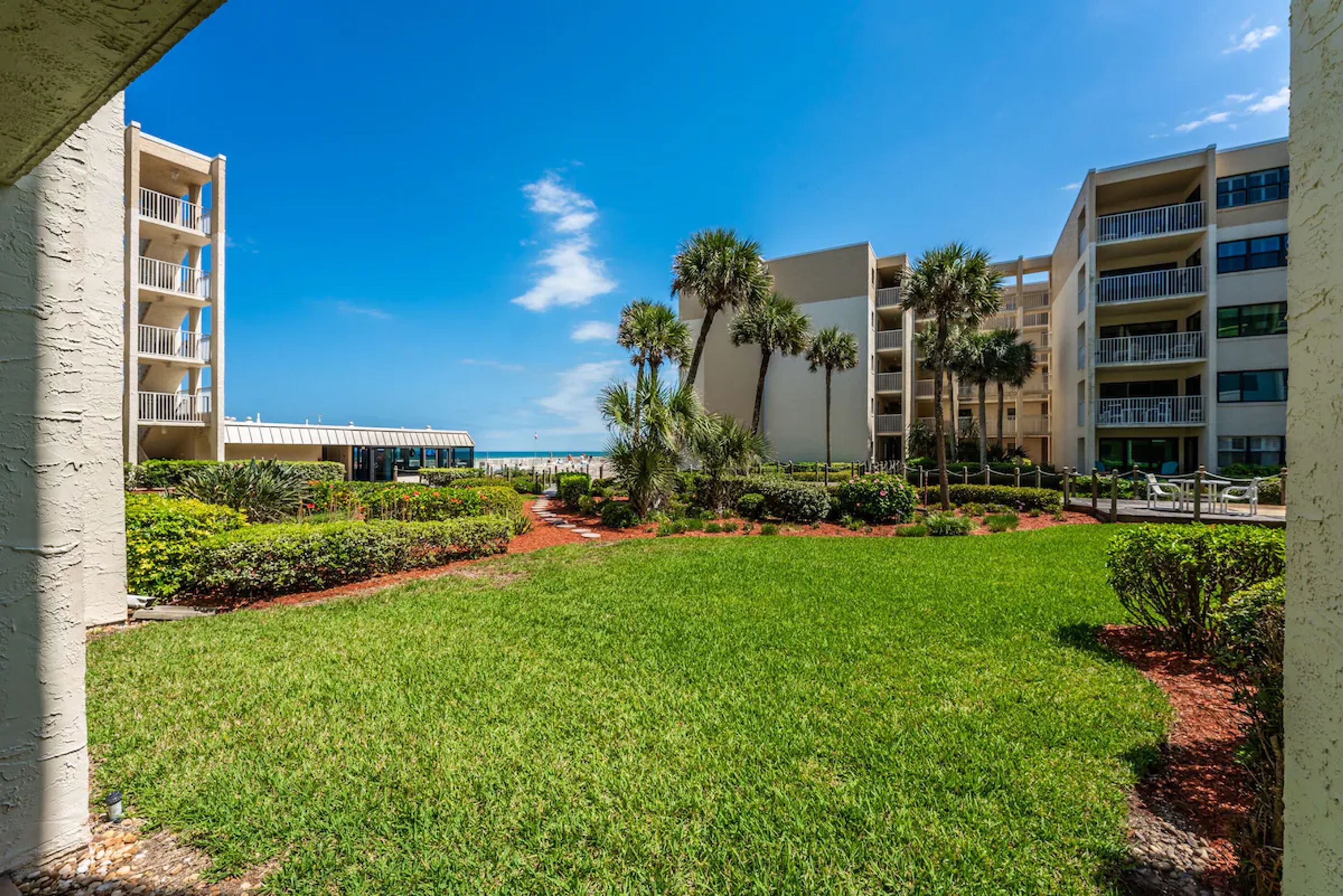 A hotel courtyard with a well-maintained lawn, palm trees, and a pool area.