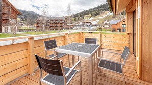 A wooden deck with a table and chairs, overlooking a mountainous area with buildings in the background. - Pleasant Apartment With Sauna (Sankt Georgen am Kreischberg)