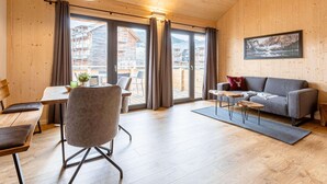 A cozy room with a wooden ceiling, a sofa, a dining table with chairs, and a view of a mountain landscape through the glass doors. - Pleasant Apartment With Sauna (Sankt Georgen am Kreischberg)