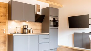 A modern kitchen with grey cabinets, a built-in oven, and a flat-screen TV mounted on the wall. - Pleasant Apartment With Sauna (Sankt Georgen am Kreischberg)