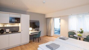 Une chambre d’hôtel compacte comprenant un coin cuisine, un lit, un bureau avec une télévision et un balcon avec vue.