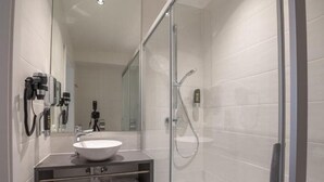 Une salle de bain moderne avec une douche à parois de verre, un lavabo blanc et un meuble-vasque avec espace de rangement pour les serviettes.