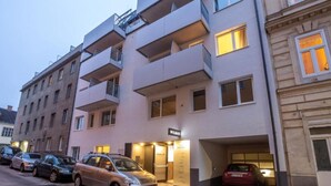 Un immeuble à plusieurs étages doté d’une architecture moderne, avec des balcons et une entrée centrale.