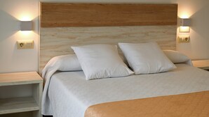 Ein ordentlich bezogenes Bett mit Holz-Kopfstück, zwei Nachttischen und Wandleuchten.