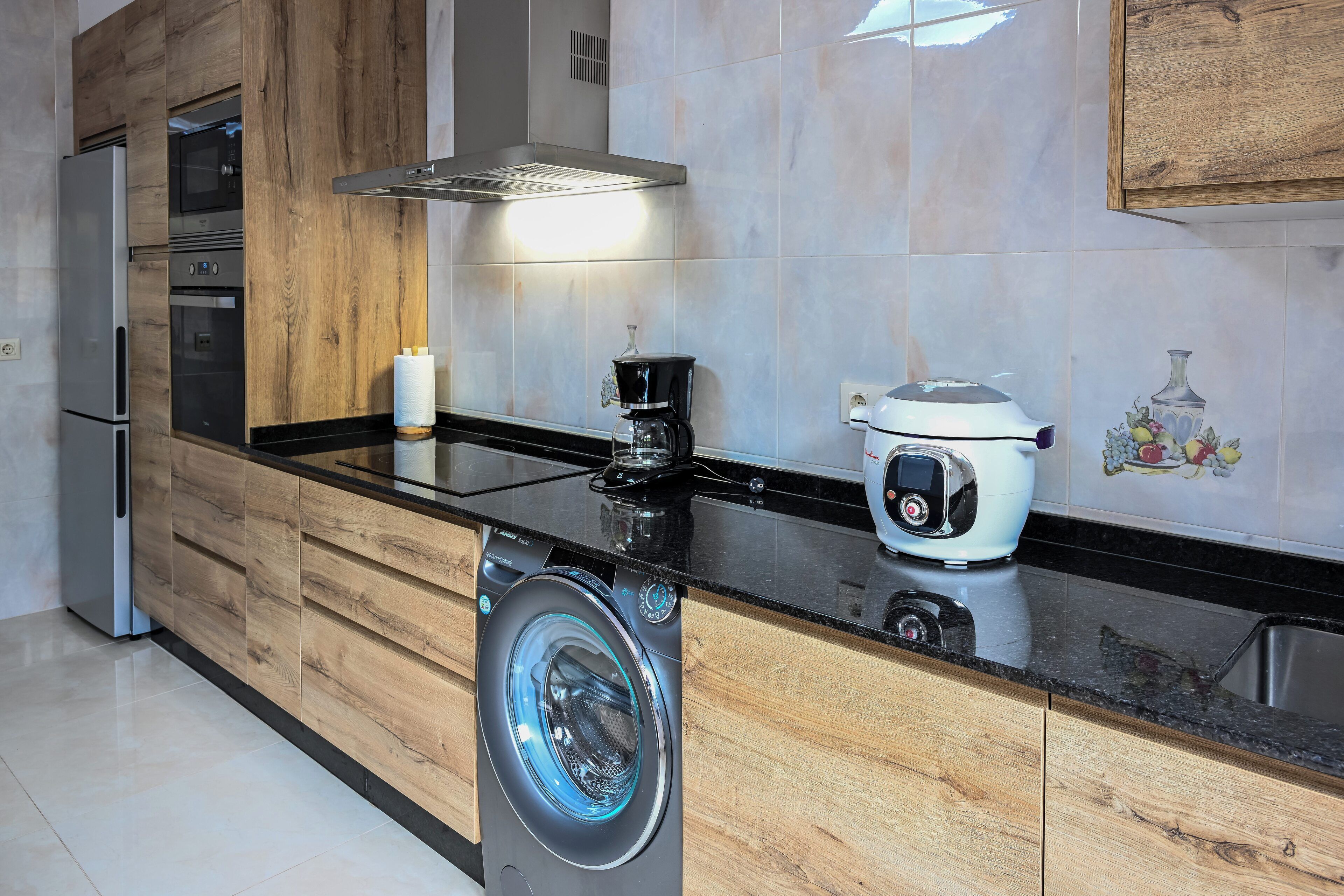 A modern kitchen with wooden cabinetry, a built-in washing machine, a coffee maker, and a toaster.