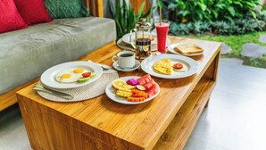 A breakfast setup with plates of eggs, toast, and fruit, a coffee pot, and a glass of juice on a wooden table. - Sawitri Anandhita Luxury Villas (Ubud)