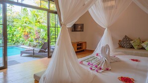 A bedroom with a large glass door leading to a pool area, a bed with white bedding and a canopy, and a small wooden side table. - Sawitri Anandhita Luxury Villas (Ubud)