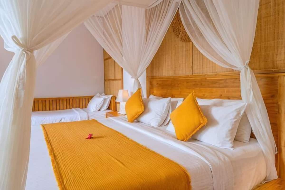A room with a wooden headboard, two beds with white bedding and yellow pillows, and a yellow throw blanket.