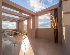 Un balcon spacieux offrant une vue dégagée sur le ciel, une chaise blanche et une plante en pot.