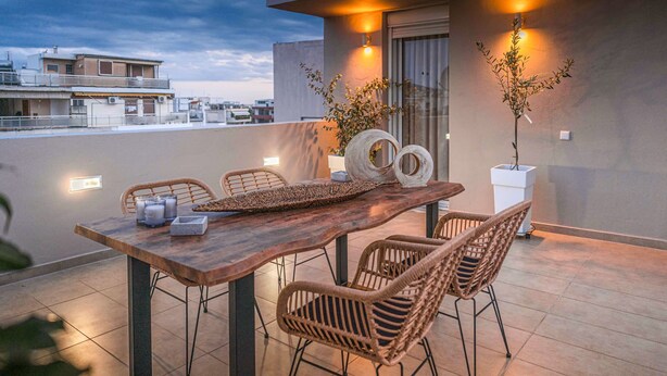 Una terraza en la azotea con una mesa de madera, sillas de mimbre y plantas en macetas.