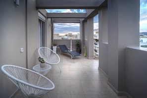 Un balcon avec deux chaises en osier blanc, un fauteuil et une petite table sur laquelle est posée une plante en pot.