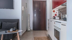 Una cocina moderna con armarios blancos, un revoque rojo y un horno empotrado. Se ve una puerta de madera que da a otra habitación y una pequeña mesa con un florero y una vela.