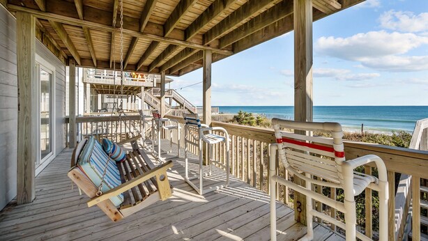 A wooden deck with a swing chair and a bench, overlooking a beach.