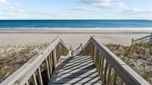 A wooden boardwalk leading to a beach with a clear view of the ocean.