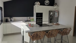 Una cocina moderna con una isla central, taburetes de bar, un salpicadero negro y un refrigerador de acero inoxidable.
