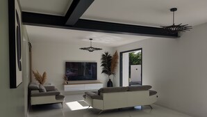 Una sala moderna con dos sofás, un televisor de pantalla plana grande, una planta decorativa y vistas a través de una puerta abierta.