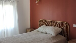 Un dormitorio con una cama grande, una mesita de noche, una lámpara de pared y un ventanal con cortinas.