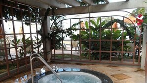 A hot tub with a metal railing, surrounded by a tiled floor and a metal fence with plants. - Ap Completo Parq. Aquát. Incrível Grátis (Caldas Novas)