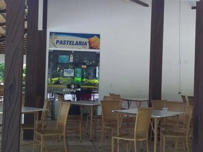 An outdoor seating area with tables and chairs, a pastelaria vending machine, and a view of the outdoors. - Ap Completo Parq. Aquát. Incrível Grátis (Caldas Novas)