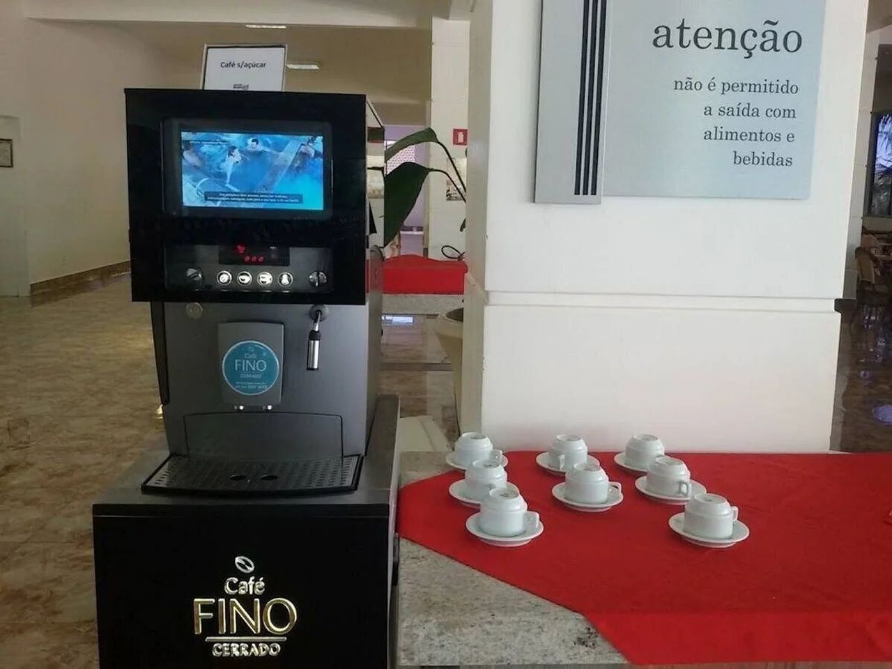 Une machine à café dotée d’un écran, une pancarte indiquant « Café Fino fermé », et une table avec des tasses blanches.