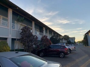 Un hôtel à plusieurs étages doté d’un parking, où l’on peut voir une rangée de voitures garées et un ciel dégagé.