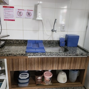 A kitchen with a granite countertop, a sink, a faucet, and a soap dispenser. There are signs on the wall and a shelf with containers below the countertop.