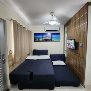 Een kamer met een bed, een plafondventilator, een airconditioner, een televisie en een houten wand.