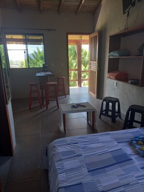 Relax in this cozy space with a comfortable bed, a small table, and a view of lush greenery outside.
