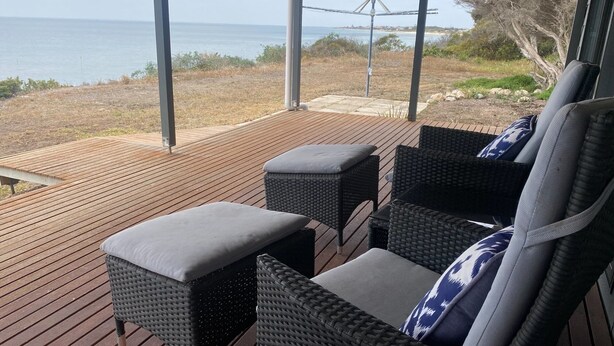 A covered outdoor seating area with wicker furniture and cushions, overlooking a beach and ocean. - Hendys 346 - Absolute beachfront! Excellent sea views! (Point Turton)
