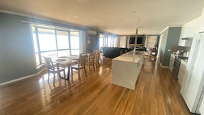 A spacious living area with a dining table, chairs, a sofa, and a kitchen with white cabinets and a central island. - Hendys 346 - Absolute beachfront! Excellent sea views! (Point Turton)