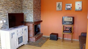 Una sala de estar con chimenea de piedra, televisor y una máquina de coser sobre un soporte de madera.