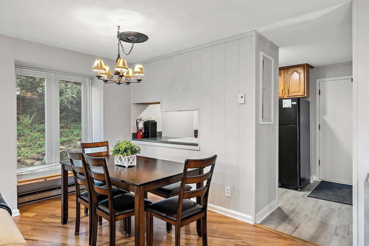Une cuisine moderne avec des meubles blancs, un réfrigérateur noir et un coin repas comprenant une table et des chaises en bois.