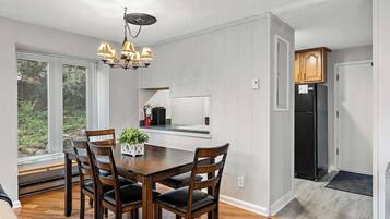 Une cuisine moderne avec des meubles blancs, un réfrigérateur noir et un coin repas comprenant une table et des chaises en bois.