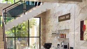 Un interior moderno con una pared de mármol, un sofá, una mesa de centro, una escalera y un letrero que dice "VITAMIN BAR".