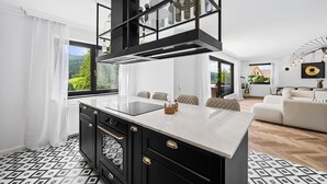 Cozinha moderna com ilha central, armários pretos e vista para o exterior através de amplas janelas.