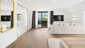 Uma sala de estar moderna com um sofá grande branco, uma parede espelhada e vista para uma floresta através de amplas janelas.