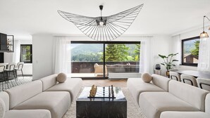 Uma sala de estar moderna com uma janela grande, um lustre e um tabuleiro de xadrez sobre uma mesa de centro preta.