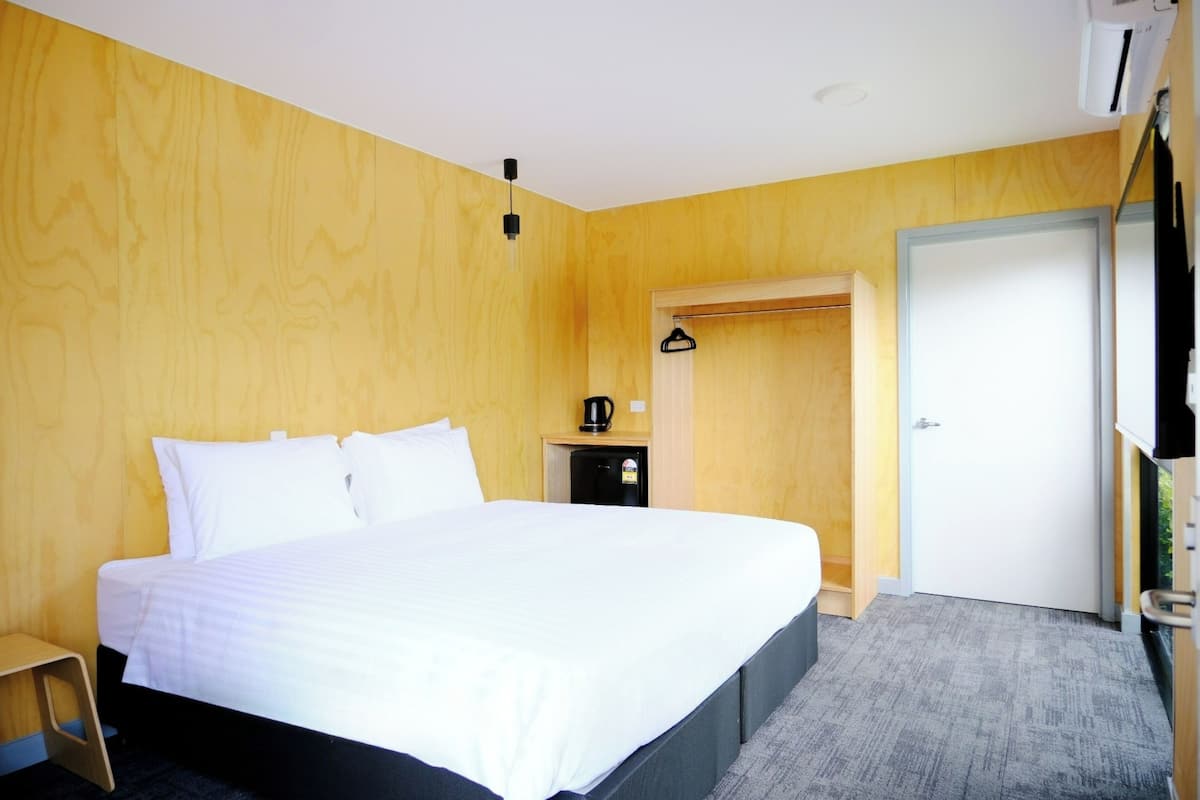 Une chambre d’hôtel avec un grand lit, une petite table de chevet avec une machine à café, une armoire et une porte donnant sur une autre pièce.