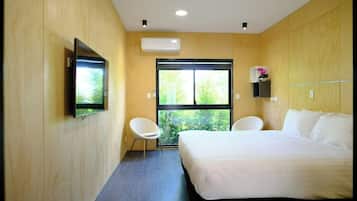 Een moderne hotelkamer met een groot bed, een flatscreen televisie aan de muur, een raam met uitzicht op groen en een klein plankje met een vaas.
