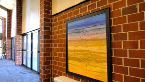 A corridor with brick walls and framed artwork depicting a landscape. - Gallery Hotel Manjimup (Manjimup)