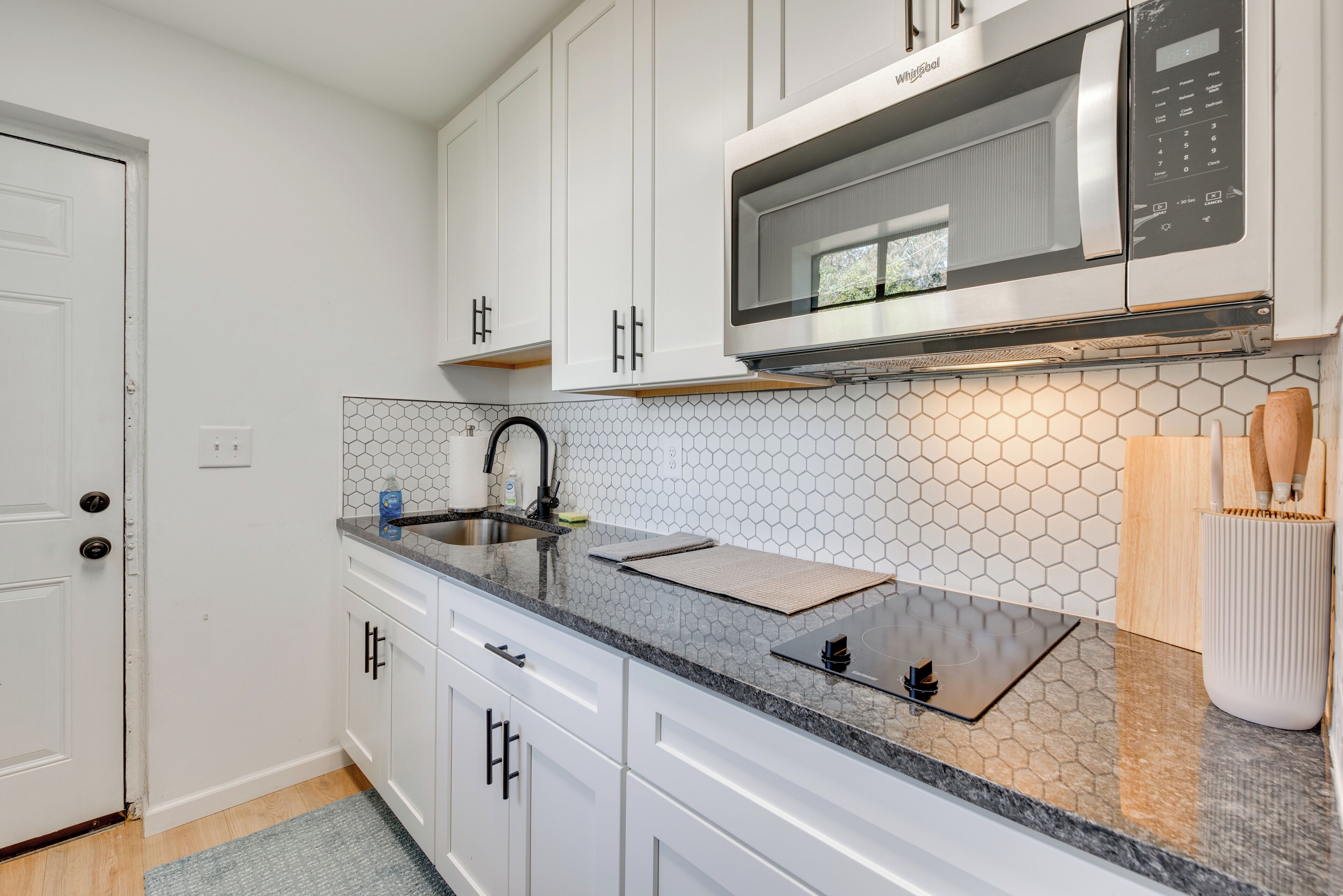 A modern kitchen with white cabinets, a microwave, and a hexagonal tile backsplash.